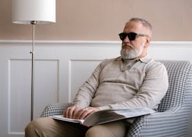 Senior man with sunglasses reading a braille book in a cozy modern interior.